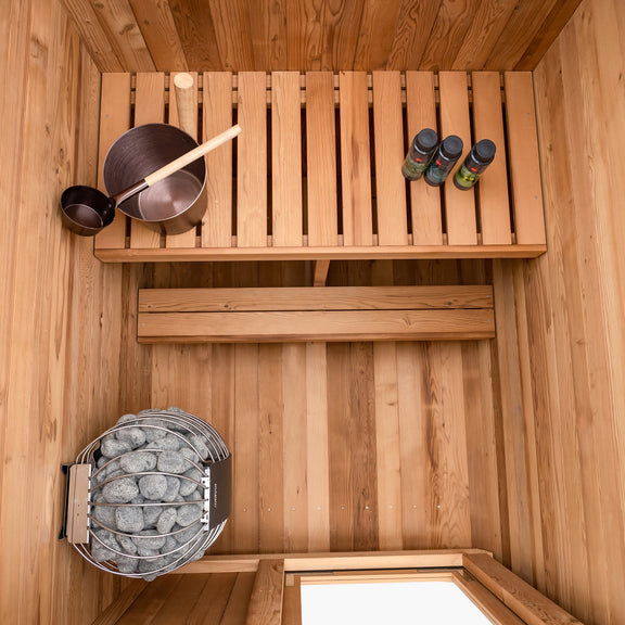 Wooden sauna interior with a shelf, stones, and containers.