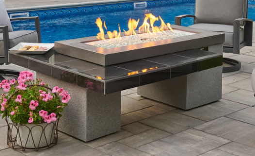 Outdoor fire pit table with flames on a patio near a pool